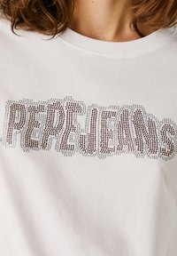 Vit bomull T-shirt med en texturerad, med rhinestones prydd "PEPE JEANS"-logotyp i gradientfärger. Klassisk rundhalsad design.