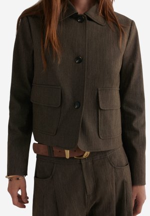 Bruine tailor jacket met een kraag, voorzien van twee voorzakken en knoopsluiting, gemaakt van een gestructureerde stof.