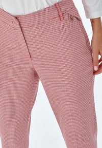 Pantalons ajustés à carreaux rouges et blancs avec une texture lisse, dotés d'une fermeture à bouton sur le devant et de poches latérales.