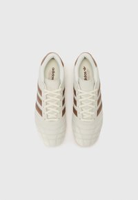 Beige sneakers med brune læderdetaljer og tre hvide striber. Struktureret overdel og flade snørebånd. Klassisk design med rund tå.