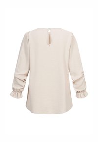 Blusa beige chiaro con maniche a sbuffo, polsini arricciati e chiusura a occhio di bue sul retro. Il tessuto testurizzato spicca in un design a vestibilità rilassata.
