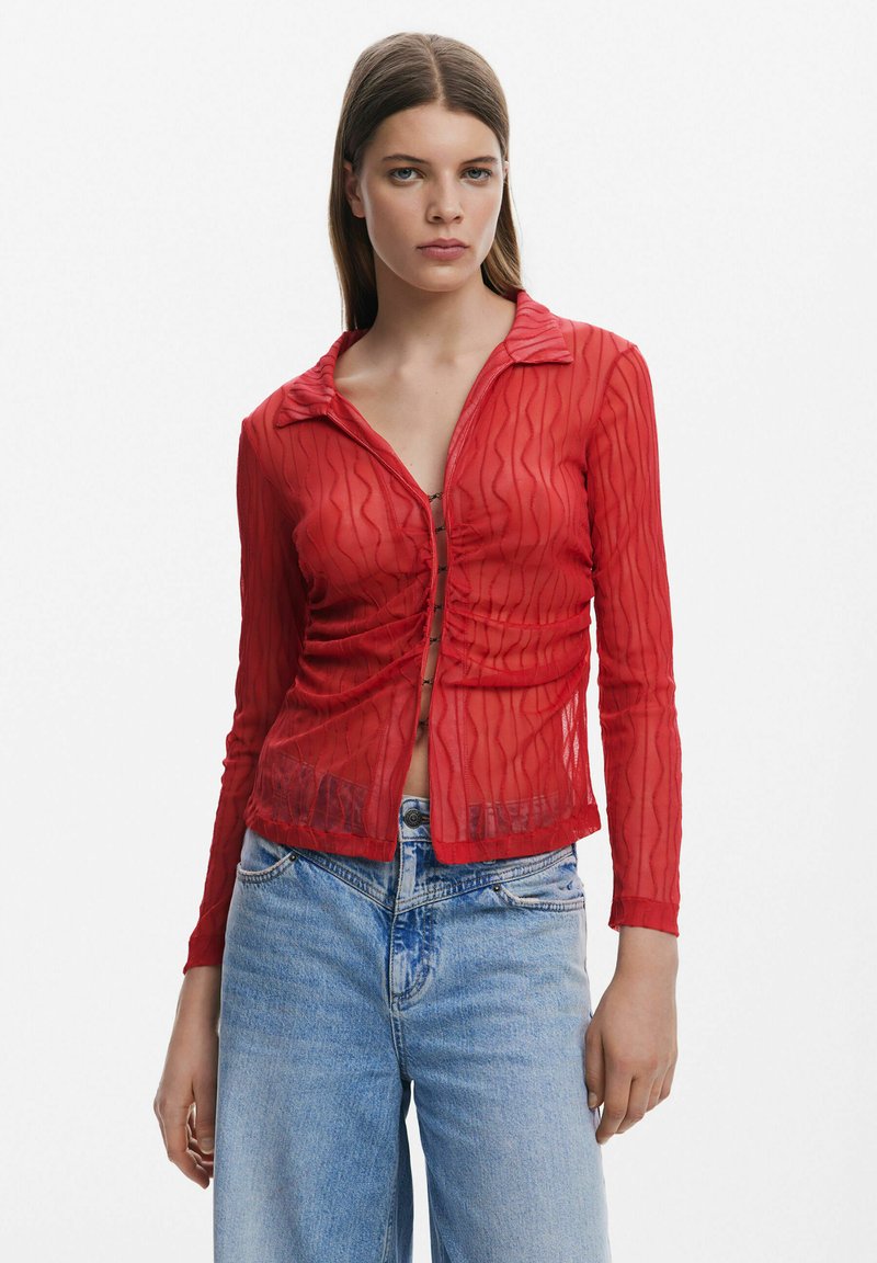 Rotes, durchsichtiges Langarmhemd mit einem strukturierten Wellenmuster, ausgestattet mit einem Kragen und einer Knopfleiste vorne, kombiniert mit hellblauen Jeans.