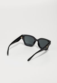 Lunettes de soleil noires en forme d' œil de chat, finition brillante, verres gris, et côtés texturés noirs avec des accents en métal doré.