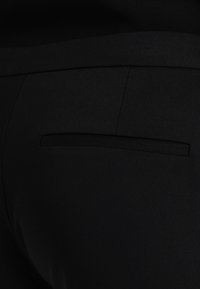 Pantalons noirs avec une texture lisse et une coupe ajustée. Présente une seule poche arrière avec un design passepoilé.