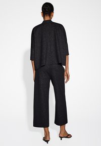 Zwarte outfit met een losse, boxy top en wijde broek, beide met een subtiele gestructureerde textuur, die de vloeiende ontwerpen aanvullen.