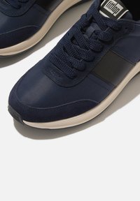 Marineblauwe sneakers met een textiel bovenwerk, contrasterende suède accenten en een ronde witte rubberen zool. Voorzien van een klassieke vetersluiting.