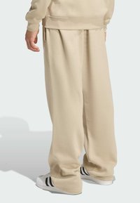 Beżowe spodnie dresowe o luźnym kroju, z plisami i elastycznym paskiem, zestawione z białymi trampkami w czarne paski.