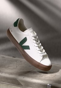 White leather sneaker with green V logo and accents, white laces, and brown rubber sole. Smooth texture with subtle stitching details.