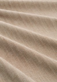 Beiger Fischgrät-Stoff mit subtiler Glanz, der ein sich wiederholendes V-Muster aufweist, eine glatte Textur und einen weichen Fall hat.
