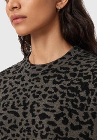 Close-up van een vrouw die een zwart-grijze luipaardprinttrui draagt en een kleine zilveren ringoorbel in haar linkeroor heeft.