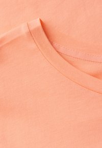 Hodno tkanina z broskvovou barvou vyrobená z bavlny, se zaobleným výstřihem s ribovým lemováním, hladkou texturou a jednoduchým designem.