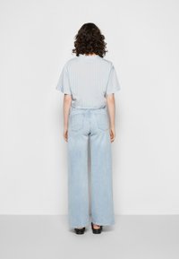 Camisa de manga curta às riscas azul-claro combinada com jeans de ganga azul-claro de perna larga e cintura alta, com bolsos traseiros e bainha limpa.