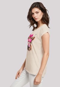 Beige cotton t-shirt featuring a graphic of a cartoon animal with pink sunglasses and a bow, short sleeves, and a relaxed fit.