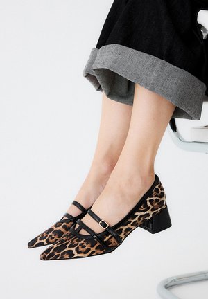 Zapatos de tacón de estampado de leopardo con punta afilada, acentos negros, doble correa y un tacón ancho; los materiales combinan tela y cuero sintético.