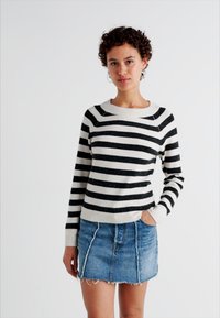 Zwart-wit gestreepte trui met een boot-halslijn, gecombineerd met een denim minirok met rafelige randen en naden op het voorpaneel.