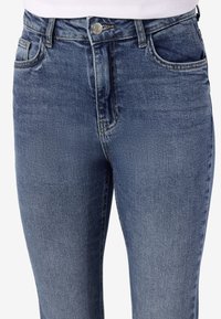 Plave traperice visokog struka s pet džepova, metalnim zakovicama i blago izblijedjelom teksturom.