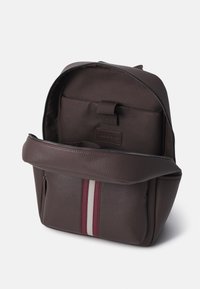 Sac à dos en cuir marron avec une finition texturée, doté d'une fermeture zippée et d'un accent extérieur de rayures bordeaux et blanches.