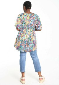 Tunique multicolore avec des motifs de papillons et de fleurs, à manches courtes, coupe décontractée, associée à un jean bleu clair et des sandales compensées beiges.