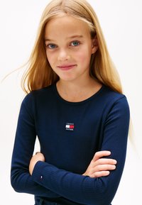 Temno modra dolgoročna majica z rebrastim vzorcem, na prsih je majhna rdeče-bela značka s logotipom Tommy Hilfiger; mehka tkanina z okroglim izrezom na vratu.