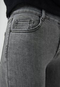 Jeans de mezclilla gris con un diseño ajustado, que cuentan con un bolsillo trasero, detalles de costura sutiles y una textura suave.