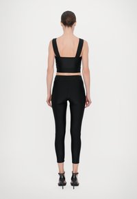Top corto nero con spalline larghe, abbinato a leggings neri a vita alta. Il materiale ha una consistenza liscia e i leggings presentano un elastico con logo.