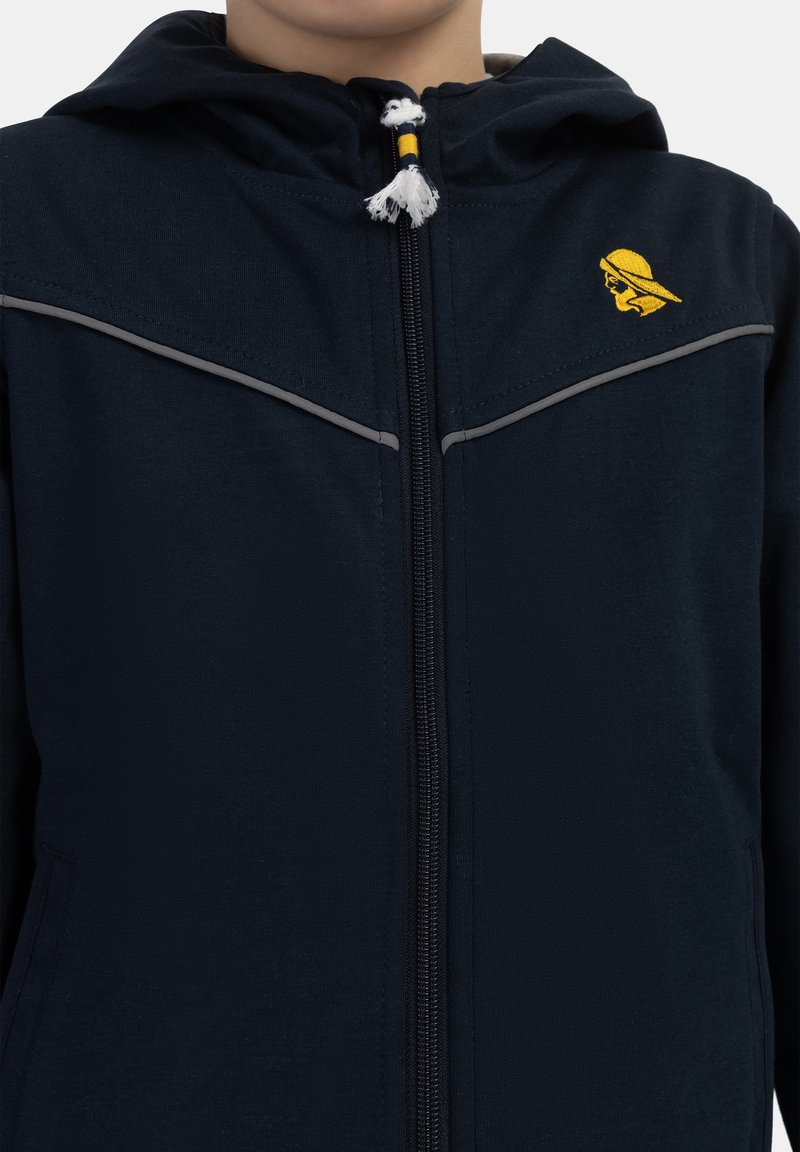 Tamsiai mėlynas užtrauktukas striukė su gobtuvu, kuriame yra šviesiai pilkos juostelės, geltonas logotipas ant krūtinės ir tekstūruotas audinio paviršius.