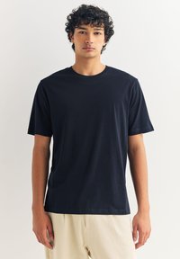 Majica tamnoplave boje s kratkim rukavima, izrađena od mekanog materijala s okruglim izrezom. Ima ležerni kroj i minimalistički dizajn bez uzoraka.