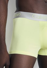 Calvin Klein boxershorts in fluorescent geel met een gladde textuur, voorzien van een zilveren tailleband met het merkje in reliëf.