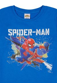 Niebieska bawełniana koszulka z grafiką Spider-Mana w akcji, z napisem "SPIDER-MAN" w białych blokowych literach nad wzorem.