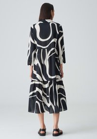 Schwarz-weiß gemustertes Kleid mit langen Ärmeln, schichtweise Rock und Kragenhalsauschnitt, aus einem leichten Stoff mit fließender Textur.