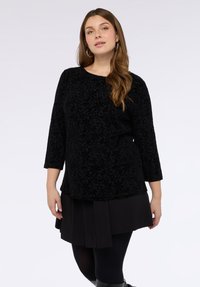 Musta pitkähihaisen paita, jossa on teksturoitu kukkakuosi, yhdistetty hameeseen, jossa on laskoksia. Ominaisuuksiin kuuluu pyöreä pääntie ja rento leikkaus.