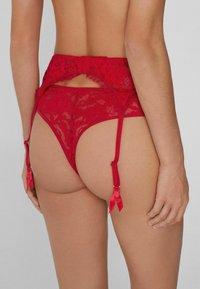 Roter Spitzenstrumpfhalter mit aufwendigen Blumenmustern, verstellbaren Trägern und Satinschleifen, entworfen im High-Waist- und offenen Rückenstil.