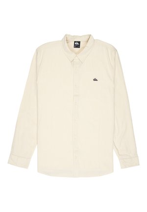 Kremowa koszula na długi rękaw z guzikami i kołnierzykiem, z małym czarnym logo na lewej piersi, rozłożona na płasko na białym tle.