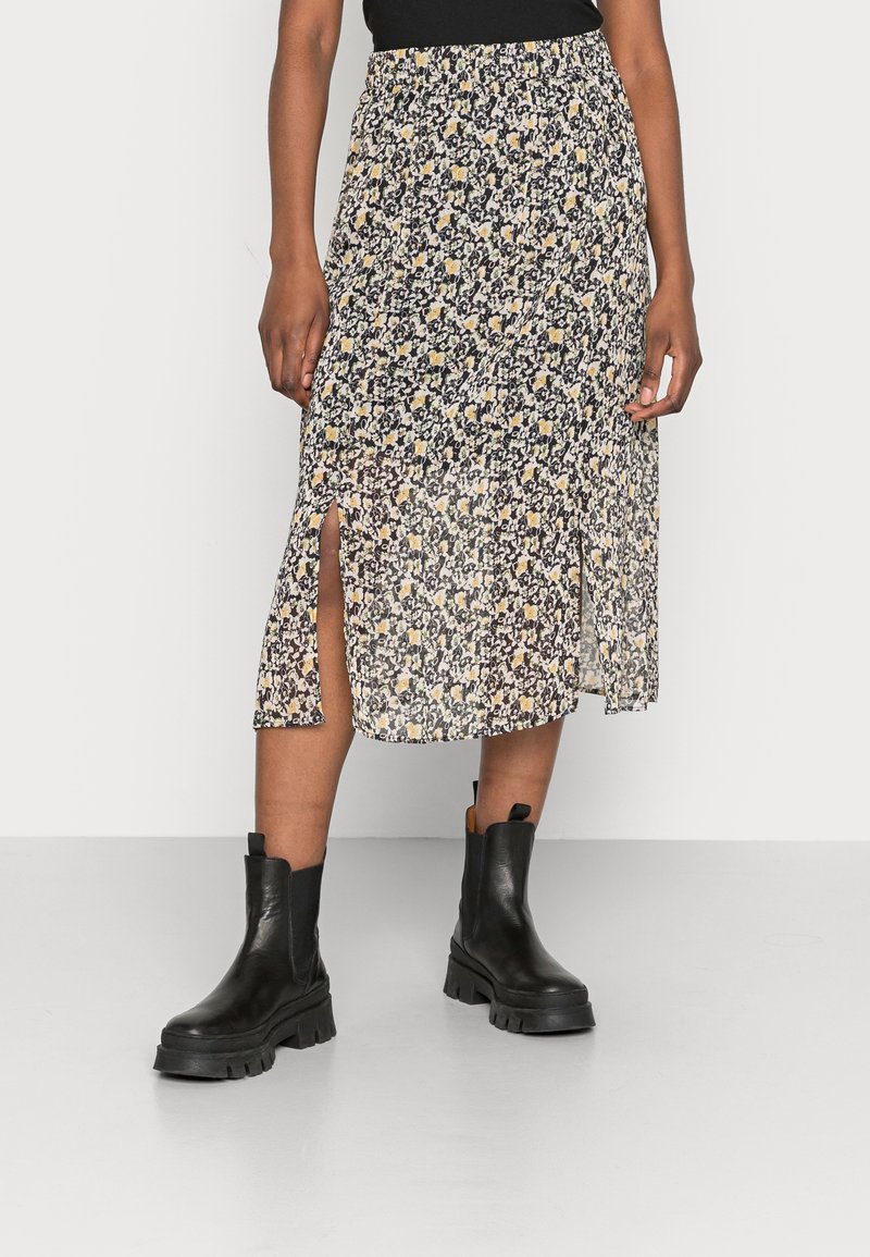 Jupe midi à motif floral avec fentes latérales portée avec des bottines noires épaisses et un top noir, visible de la taille vers le bas.