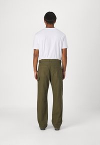 Pantalones cargo de color verde oliva con pierna recta, doble bolsillo trasero y bolsillos cargo laterales, combinados con una camiseta blanca lisa.