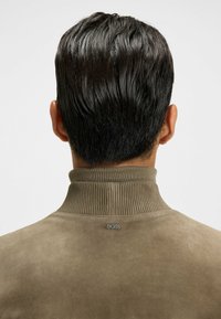 Bruine suède trui met een geribde kraag, voorzien van een klein "BOSS"-logo op de achterkant. Gladde textuur en een strakke design.