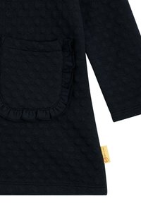 Dunkelblaues Langarmoberteil aus strukturiertem Stoff mit einer gefransten Tasche und einem gelben Markenlabel am seitlichen Saum.