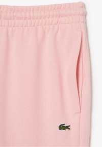 Pantalones de chándal rosa hechos de una tela suave, con una cintura elástica y bolsillos laterales. Incluye un logotipo bordado en verde en la parte inferior de la pierna.