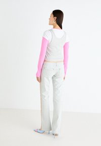 Camiseta sin mangas de color gris claro superpuesta sobre una camisa de manga larga blanca con mangas rosas, combinada con unos jeans de mezclilla claros y unos tacones azules de aguja.