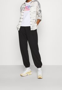 T-shirt med tie-dye i vitt och grått över en vit grafisk t-shirt. Svarta joggers med elastiska muddar och vita sneakers med gula accenter.