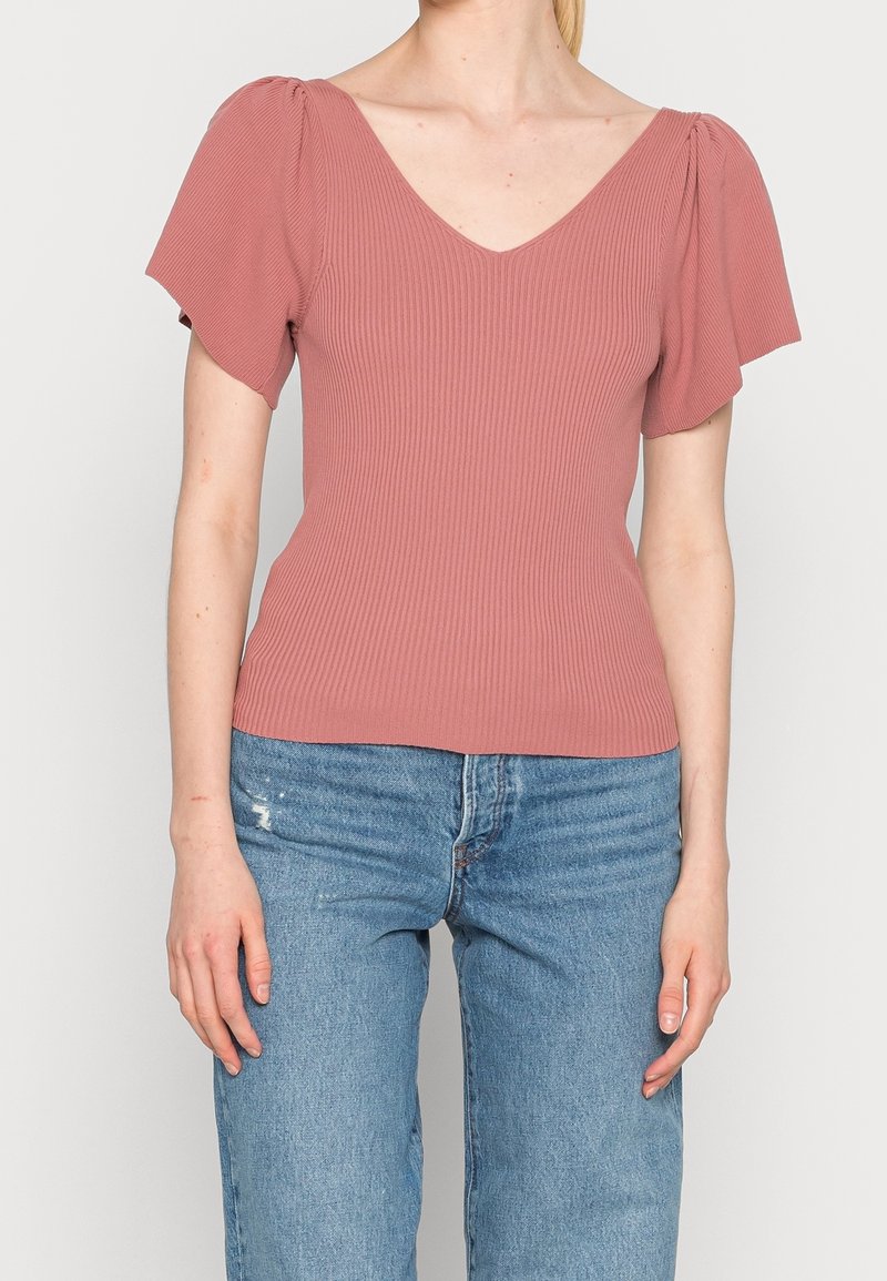 Haut côtelé rose avec manches courtes bouffantes et décolleté plongeant, associé à un jean droit bleu clair.