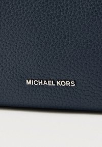 Torba za rame od tamnoplave teksturirane kože s srebrnim logotipom "MICHAEL KORS" na prednjoj strani, naglašavajući minimalistički dizajn i kvalitetan materijal.