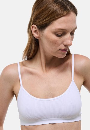 Bralette blanc côtelé avec fines bretelles, présentant une surface texturée et un bord festonné. Design simple, idéal pour superposer ou porter au quotidien.