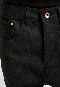Black denim pants with a straight-cut design. Features copper hardware, marked stitching, and a side pocket. Smooth texture.