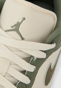 Sneaker met een bovenwerk van crème canvas met olijfgroene leren accenten, dikke crèmekleurige veters en een groen geborduurd logo op de tong.