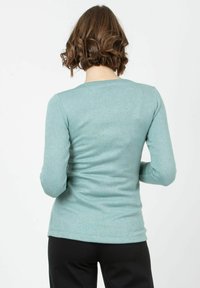 Långärmad, ljus teal-top i mjukt material, med rund halsringning och figurnära silhuett, sedd bakifrån.