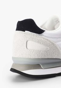 Zapatilla blanca con talón de ante gris, acentos negros, panel de malla transpirable y suela de goma estratificada para mayor estabilidad.