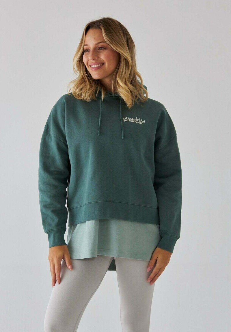 Zielona bluza z kapturem o skróconym kroju, z jaśniejszą zieloną warstwą pod spód. Miękka w dotyku, z detalem logo z przodu i sznurkami do regulacji.