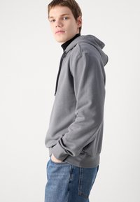 Grijze hoodie met een trekkoordcapuchon, zachte textuur, geribde mouwen en een kangoeroezak. Draag met blauwe denim jeans.