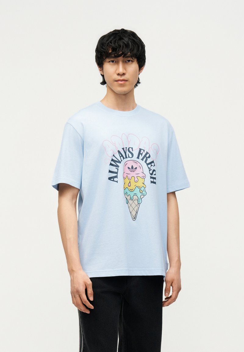 Joven con cabello negro que lleva una camiseta azul clara con un colorido cono de helado derritiéndose y el texto "Always Fresh".